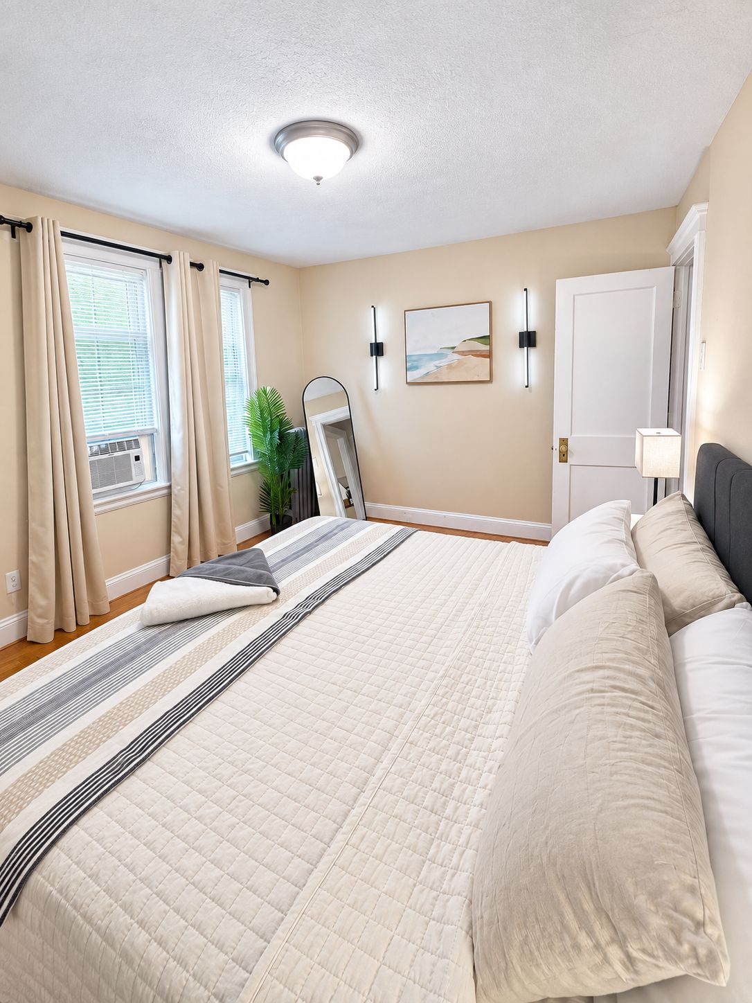 A bedroom with a large bed, a bedside table, a mirror, and a door.