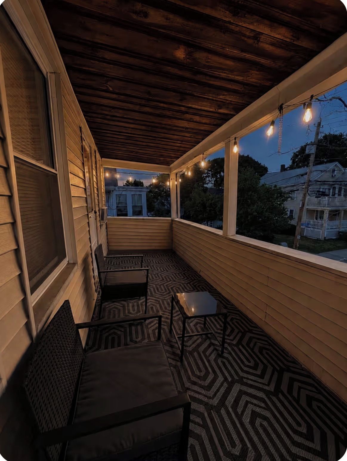 A covered porch with a patterned floor, two chairs, and string lights.