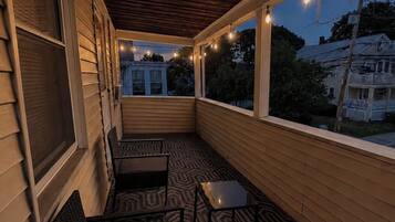 A covered porch with a patterned floor, two chairs, and string lights.