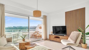Een moderne woonkamer met een grote televisie, comfortabele zitplaatsen, een balkon met uitzicht en een houten accentmuur.