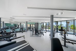 Ein modernes Fitnessstudio mit Cardiogeräten, Gewichten und großen Fenstern mit Blick auf Palmen und Gebäude.