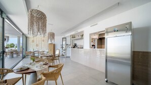 Een moderne keuken met een grote, roestvrijstalen koelkast, rieten meubels en een hangende macramé lamp.