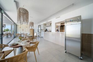 A modern kitchen with a large stainless steel refrigerator, wicker furniture, and a hanging macrame light fixture. - Oceana Gardens Apartment (Cancelada)