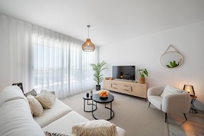 A modern living room with a sofa, coffee table, TV, and decorative plants. - Ampartment Ocena Views (Atalaya Isdabe)