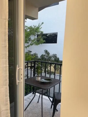 Ein Balkon mit Tisch, Stühlen, einer Topfpflanze und einem Fenster.