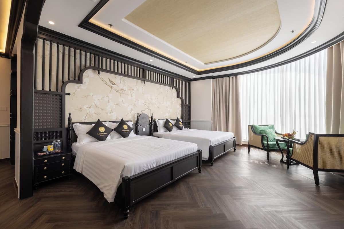 A hotel room with two beds, a green chair, a small table, and a decorative wall.