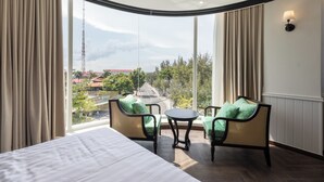 A hotel room with a large window, a bed, two chairs, and a small table.