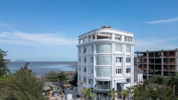 A white hotel with a curved corner, large windows, and a view of the sea.