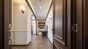 A hallway with wooden flooring, wall-mounted lighting, and a door on the right.