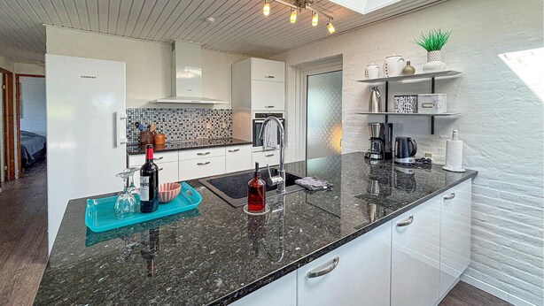 A modern kitchen with a black granite countertop, white cabinetry, and a backsplash with a mosaic pattern. - Beautiful home in Hejls with house sea view (Hejls)