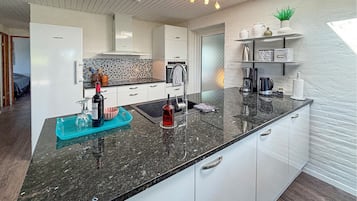 Une cuisine moderne dotée d’un plan de travail en granit noir, de meubles blancs et d’un pare-feu orné d’un motif en mosaïque.
