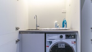 Ein kleiner Waschbereich mit Waschmaschine, Waschbecken und einer Flasche Flüssigwaschmittel.