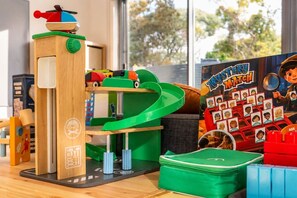 Ein Kinderspielbereich mit einem hölzernen Turm, einer grünen Rutsche und einem 'Mystery Match'-Spiel.