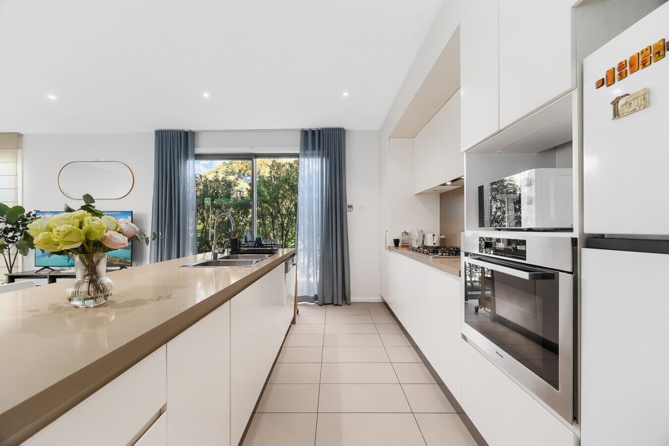 A modern kitchen with a central island, stainless steel appliances, and a view through large windows.