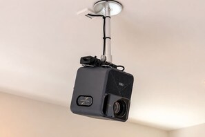 Ein an der Decke befestigter Projektor mit einer Linse und Bedienfeld, verbunden mit einem Stromkabel.