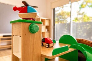 Ein Holztisch für Kinder zum Spielen mit einem grünen Stuhl, einem roten und blauen Spielikopter und einem roten Spielzeugauto.