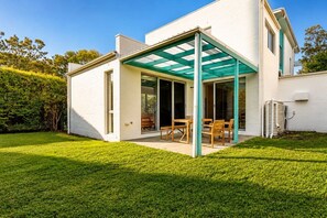 Ein modernes Haus mit überdachter Terrasse, Rasenfläche und weißer Fassade.