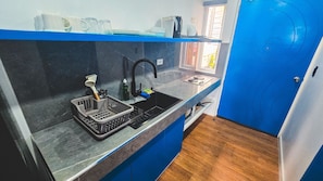 Una cocina con un lavabo negro, encimera azul y una cesta con utensilios.