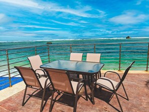 Una mesa y sillas en una terraza con vistas al océano y un promontorio rocoso.