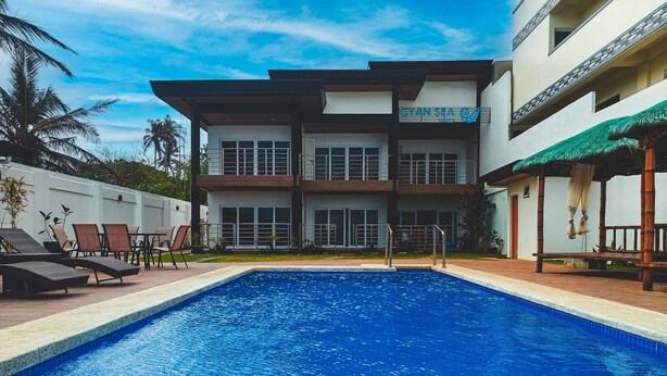 Un hotel moderno con piscina, lettini e un'area relax coperta.