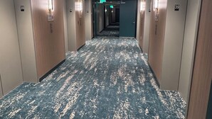 Un corridoio d'albergo con una moquette decorata, porte numerate e illuminazione a incasso.