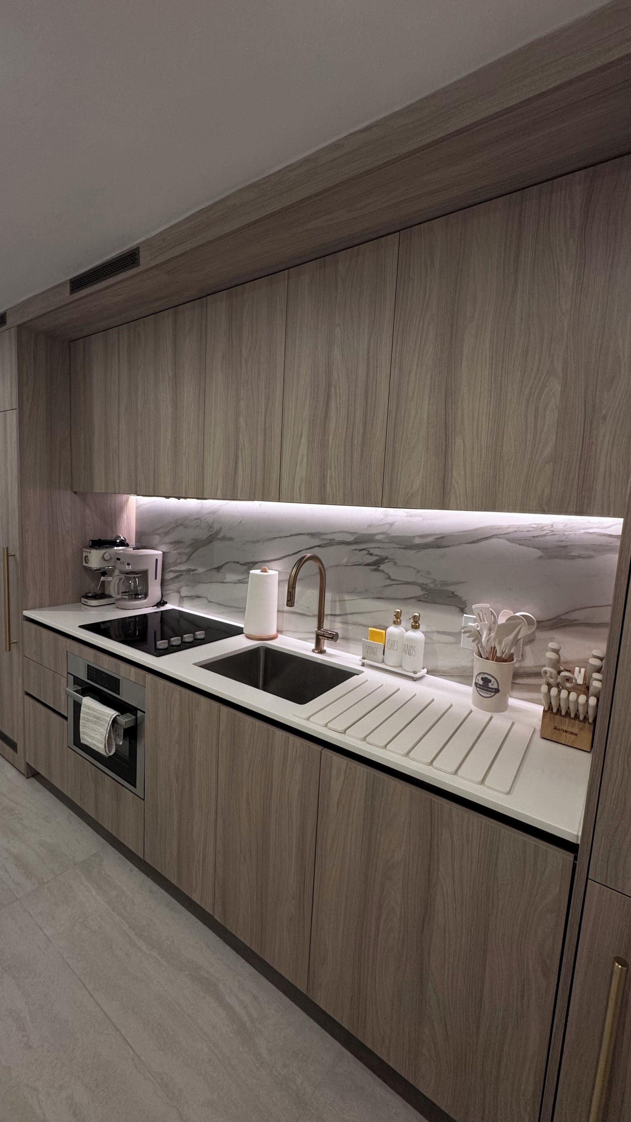 Eine moderne Küche mit Holzschränken, einer schwarzen Arbeitsplatte, einem Spülbecken, einer Kaffeemaschine und einer Marmor-Spritzschutzwand.