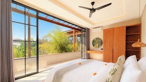 Ein Schlafzimmer mit großem Fenster, Deckenventilator, Bett mit weißer Bettwäsche und Holzschrank.
