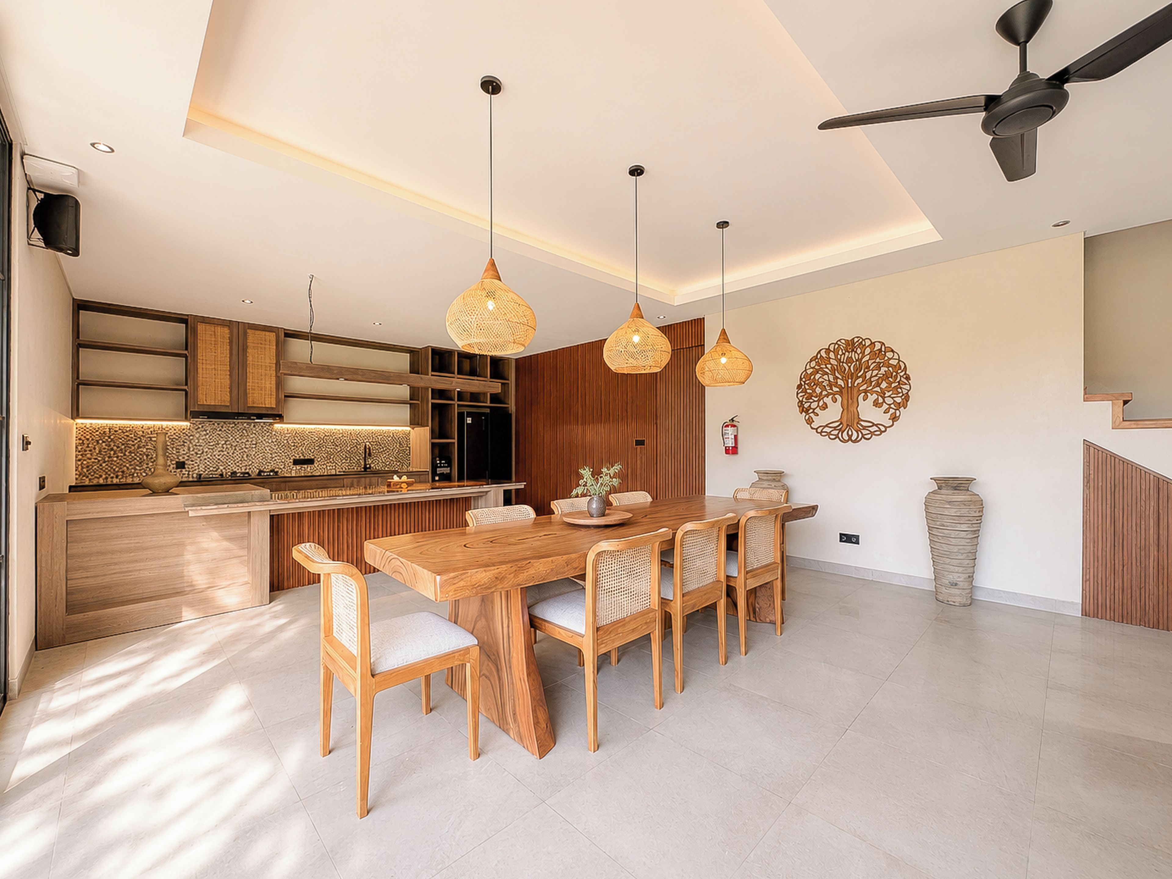 Una cocina moderna con armarios de madera, una zona de comedor con mesa y sillas de madera, iluminación colgante y un ventilador de techo.