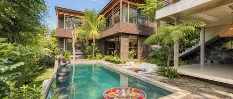 A modern resort with a pool, lush greenery, and a Buddha statue.
