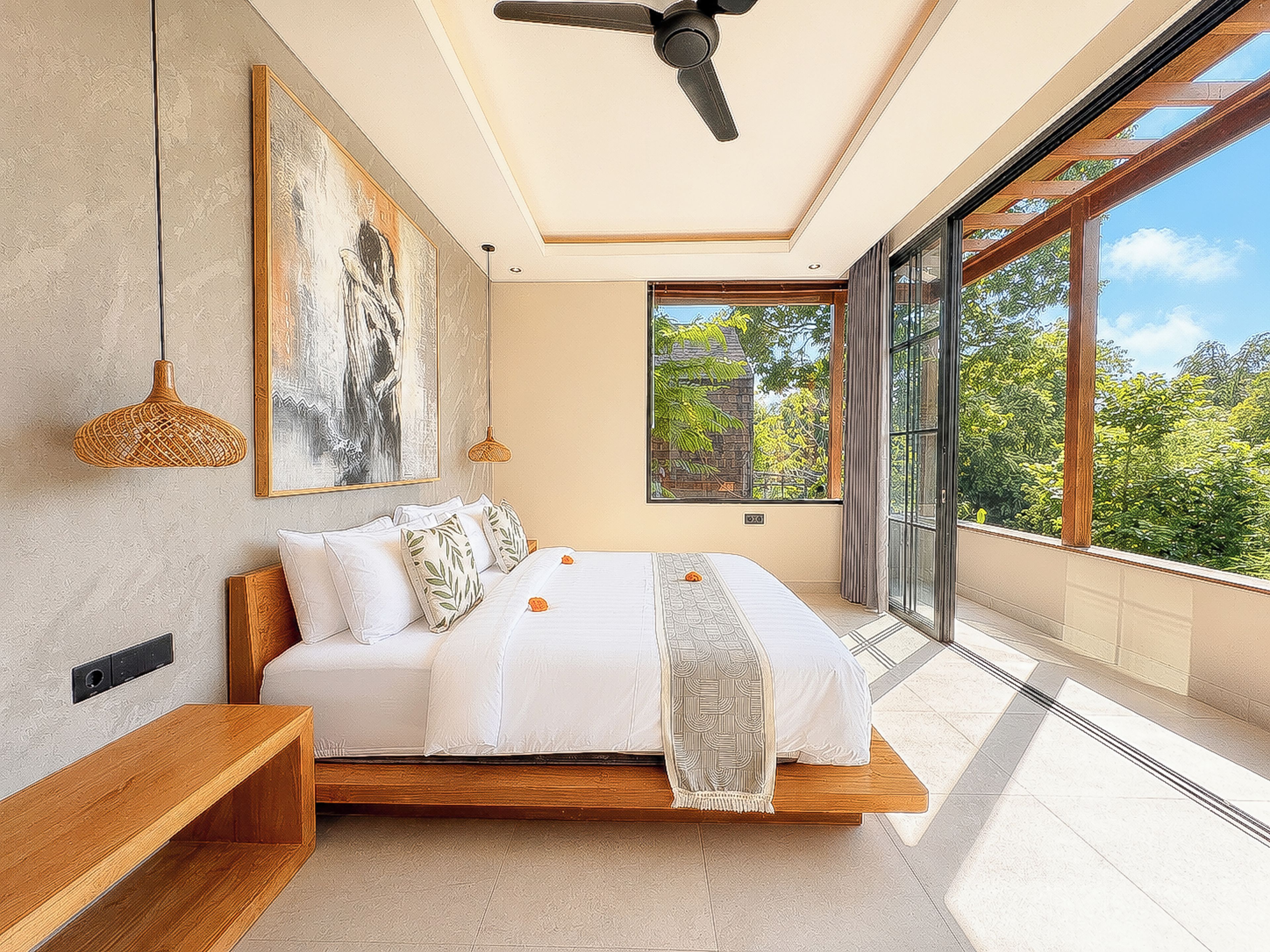 Une chambre à coucher avec un lit, un ventilateur de plafond, des œuvres d’art et une grande fenêtre donnant sur la forêt.