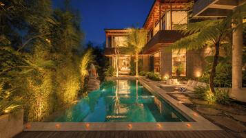 Una casa moderna con piscina, rodeada de exuberante follaje y una terraza de madera.
