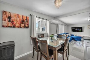 Ein modernes Wohnzimmer mit Esstisch, Stühlen, einer Couch, einem Fernseher und einem Bild an der Wand.