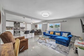 Een moderne woonkamer met een blauwe bank, een bruine fauteuil en een glazen salontafel.