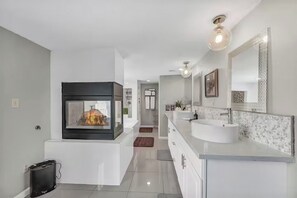 A modern bathroom with a fireplace, white vanity, and a large mirror. - Family-Friendly 4BR Home Close to Las Vegas Strip & Airport with Game Room! (Las Vegas)