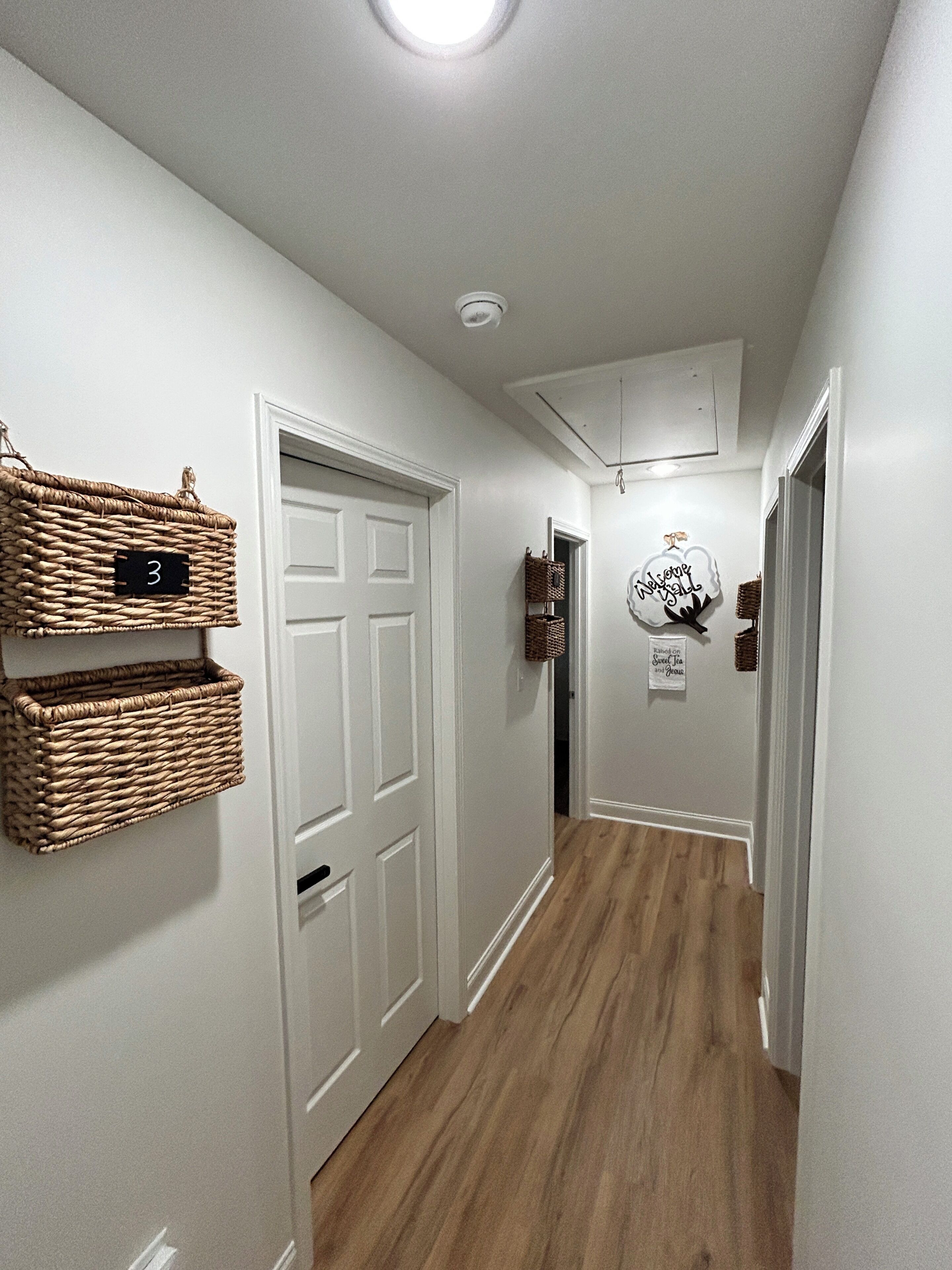 A hallway with white walls, a wooden floor, and baskets on the wall.