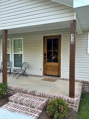 A house with a wooden door, a porch with two chairs, and a brick staircase leading to the entrance. - Welcome to Peggy’s Charming 3-bedroom house with AC in welcoming Hattiesburg (Hattiesburg)
