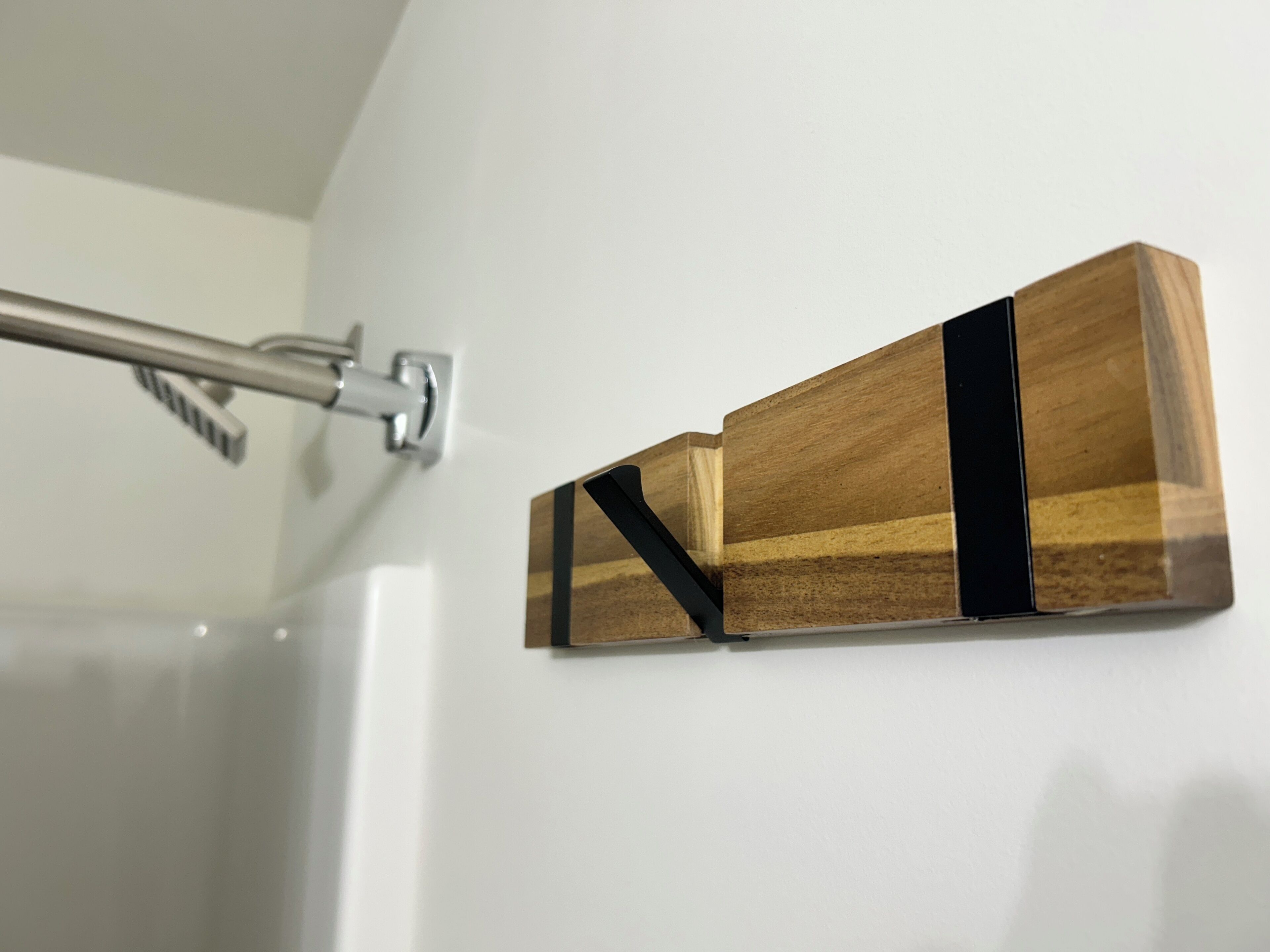 A bathroom with a shower curtain rod and a wooden wall-mounted shelf.
