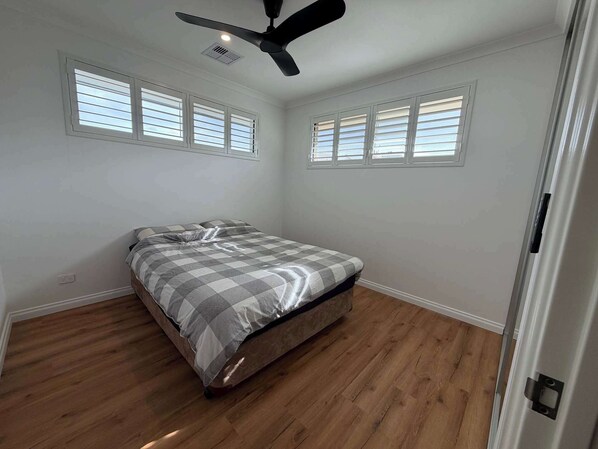 Une chambre à coucher avec un lit, un ventilateur de plafond et des fenêtres équipées de stores.