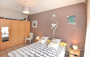 A bedroom with a bed, a wardrobe, a chair, a bedside table, and wall decorations. - Cozy home in Bagnoles (Bagnoles)