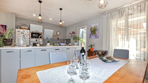 Una cucina moderna con zona pranzo, che include un tavolo in legno, bicchieri da vino, un frigorifero e illuminazione a sospensione.