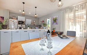 A modern kitchen with a dining area, featuring a wooden table with wine glasses, a refrigerator, and pendant lighting. - Cozy home in Bagnoles (Bagnoles)
