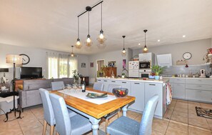 A modern kitchen with white cabinets, a dining area with a wooden table and blue chairs, and a living room with a sofa and TV. - Cozy home in Bagnoles (Bagnoles)