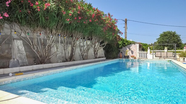 Una piscina limpida con bordo piastrellato, circondata da un basso muro in pietra e diverse piante.