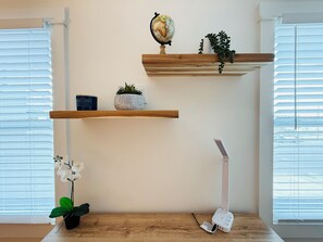 Ein Zimmer mit Schreibtisch aus Holz, einem Globus, einer Pflanze, einer Lampe und einem Fenster mit Jalousien.
