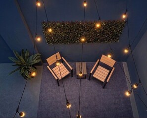 Una habitación con dos sillas de madera, una mesa pequeña, luces colgantes y una planta verde en la pared.