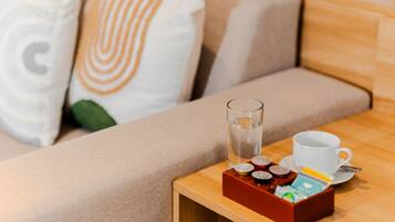 Una mesita de madera con un vaso de agua, una taza blanca y una bandeja con bolsitas de té y una caja de pañuelos.