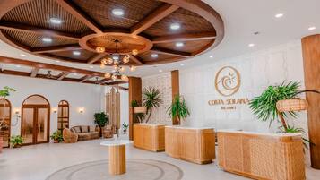 Zona de recepción con techo de madera, una mesa de recepción y un letrero en la pared para Costa Solana Resort.