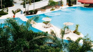 A resort pool area with multiple lounge chairs and umbrellas, surrounded by lush greenery.