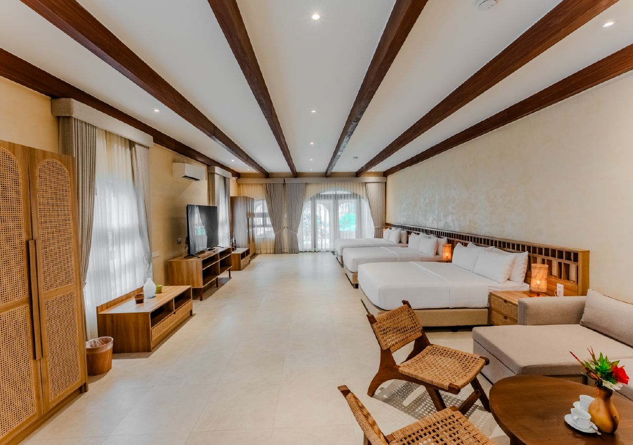 Habitación de hotel con televisión, dos camas, sofá, mesa de comedor y mueble para televisión.