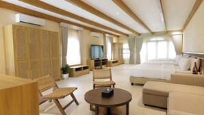 A modern hotel room with a large bed, a sofa, a dining table, wicker chairs, and a TV.